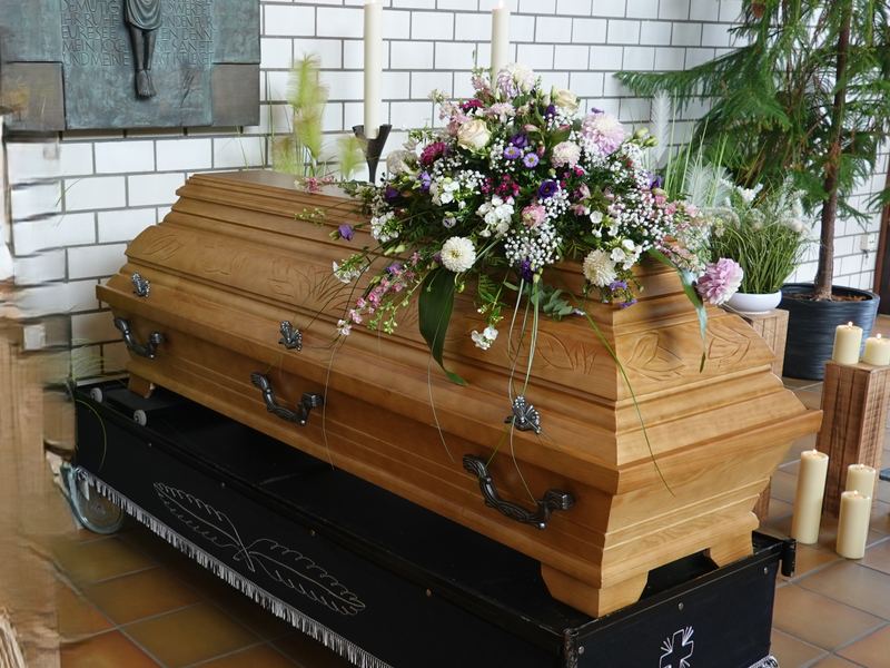 Holzsarg in warmem Braunton mit zartem Blumengesteck