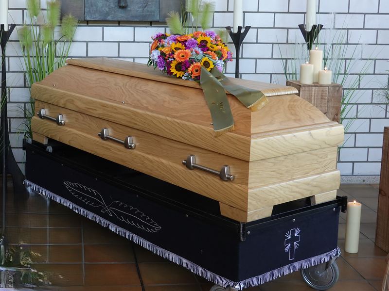 Heller Eichensarg mit buntem Blumengesteck und Schleife