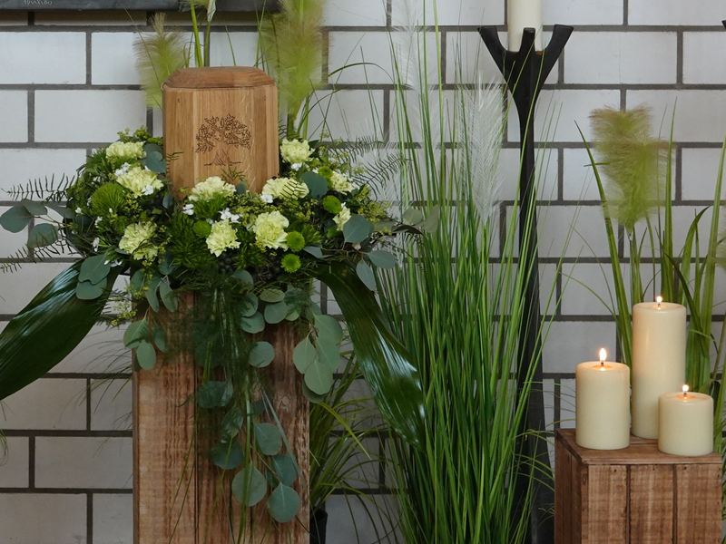 Blumengesteck mit weißen Blüten auf Holzstele, daneben Kerzen