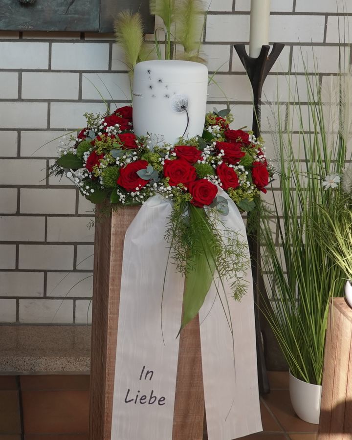 Rotes Rosengesteck mit weißer Schleife und Kerze auf Holzstele