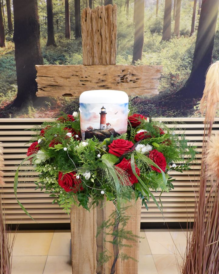 Weiße Urne mit Rosenkranz vor einem Holzkreuz